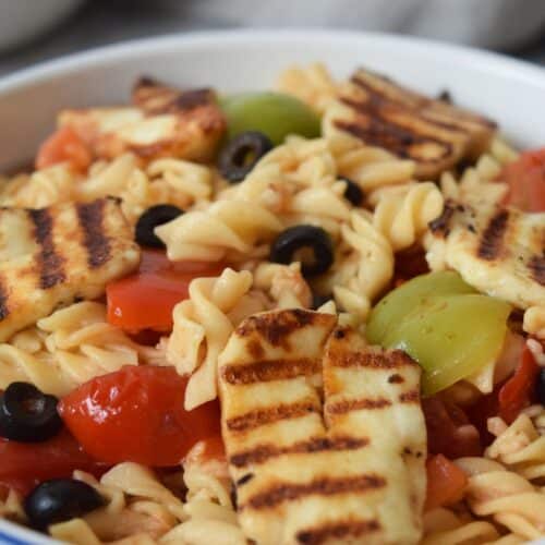 Overhead view of a low FODMAP pasta salad with brown rice noodles cucumbers and tomatoes in a ceramic bowl