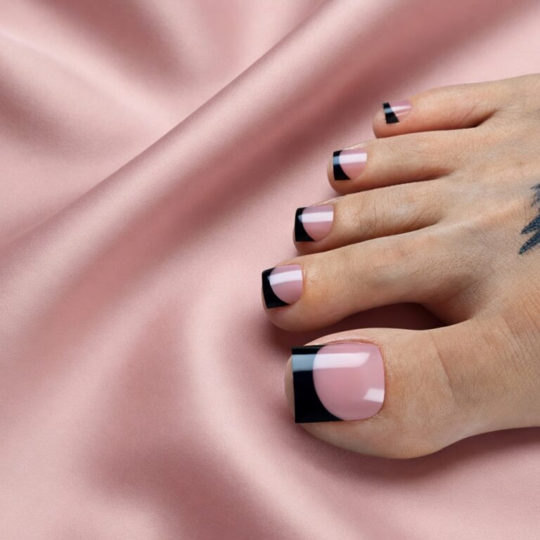 Classic black French tip toes on a sheer pink base resting on blush pink silk