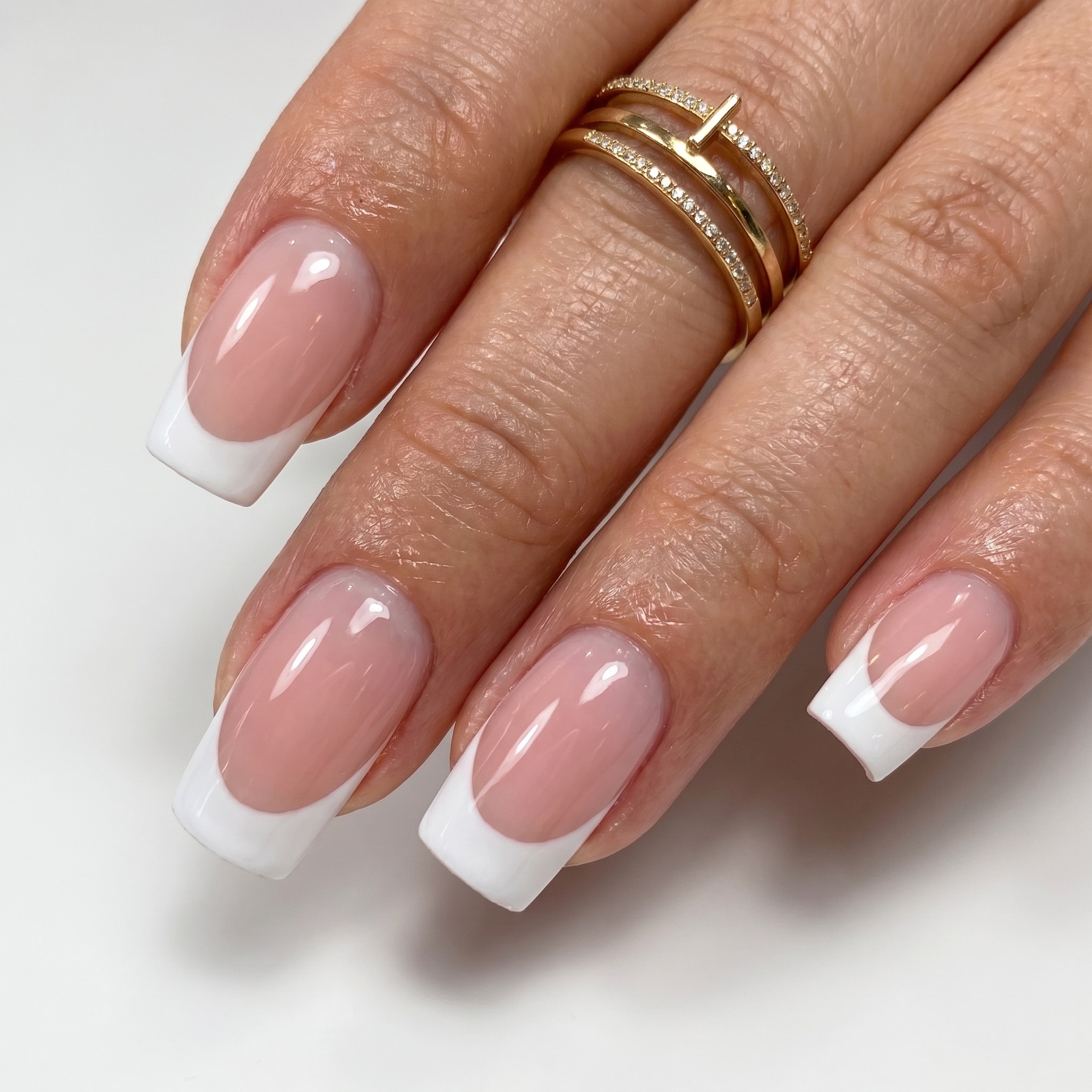 Glossy pink nude nails with soft white French tips and gold rings