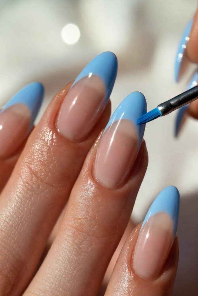 Blue French Tip Almond Nails in progress with a nude base and light blue tips being painted
