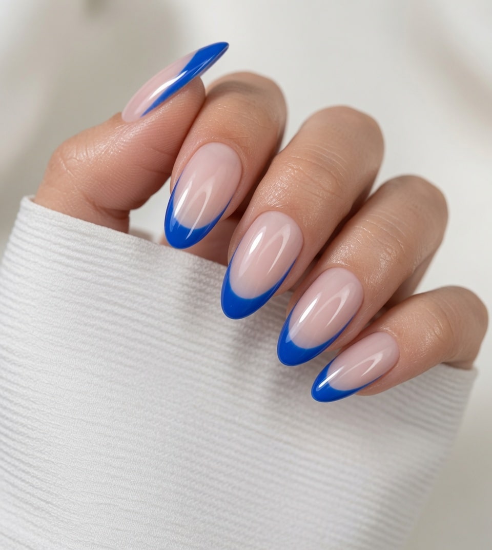 Medium almond nude nails with bold cobalt blue French tips held beside a white knit sleeve.