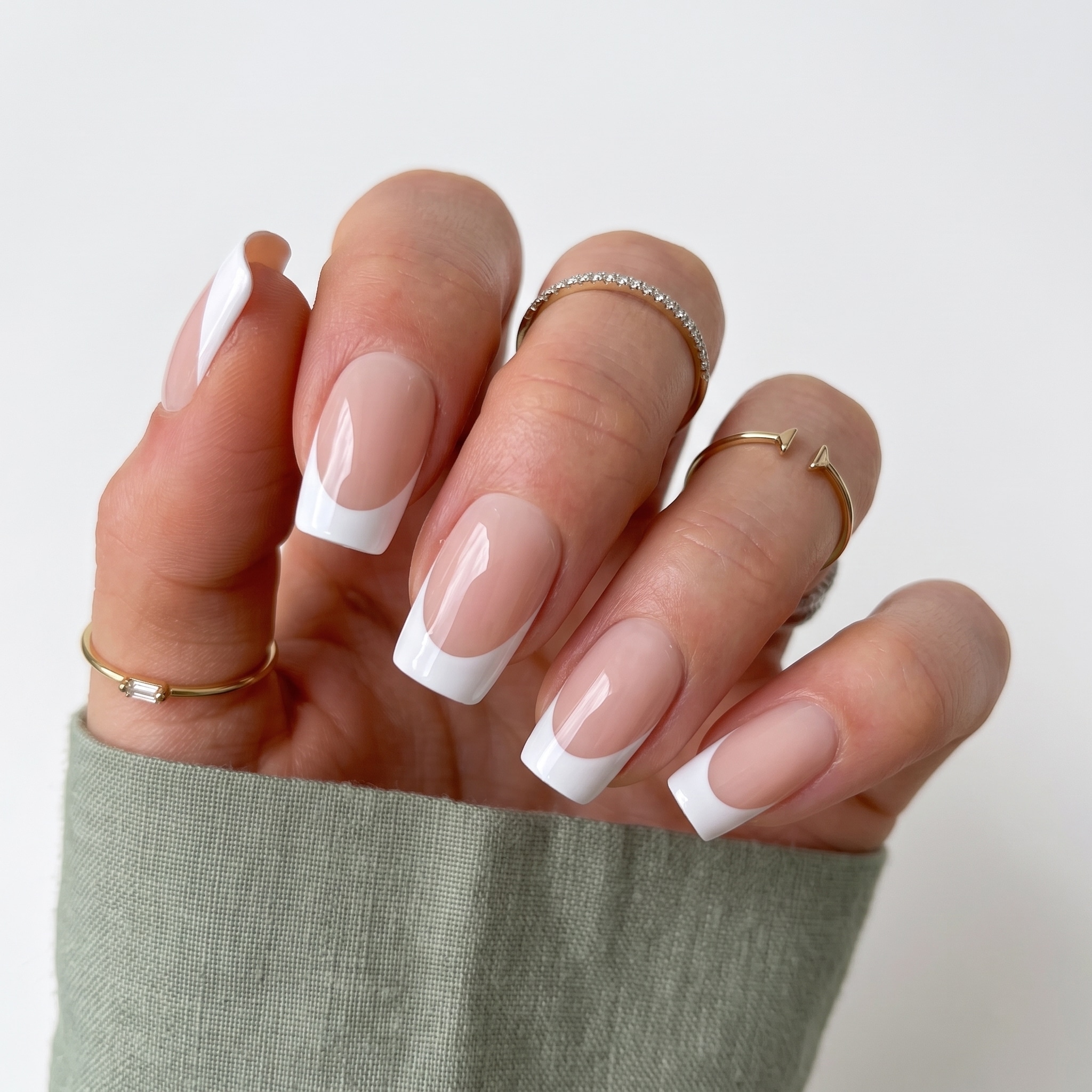 Classic white French press-ons on deep skin tone with a warm sweater sleeve and gold rings.