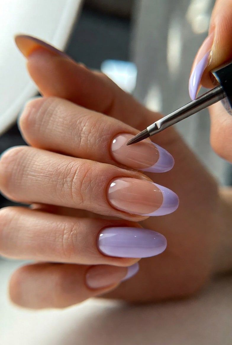 Light purple almond French tip nails in progress with a nude base and lavender tips being painted