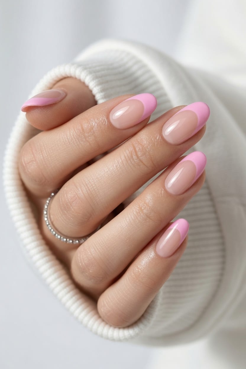 Hand with gold rings showing off a glossy pink French press-on manicure.