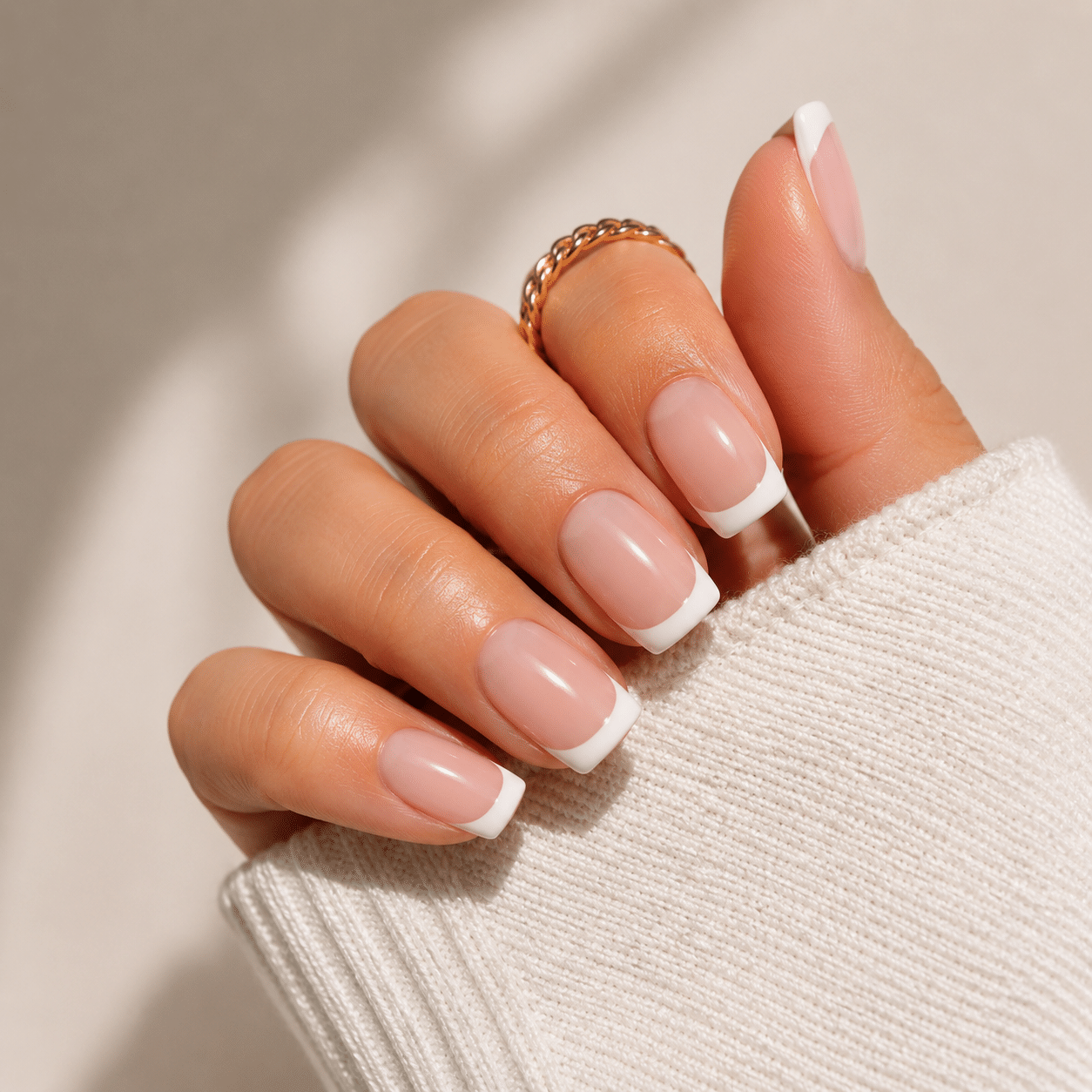 Short French tip nails with a glossy nude base and slim white tips in a cozy close-up pose