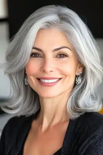 Layered Medium-Length Cut with Flipped Ends Haircut on a smiling woman with silvery gray hair.