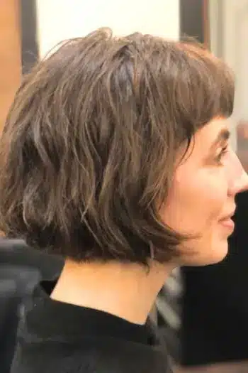 Wispy French bob with shaggy layers on a woman with brown hair, side view