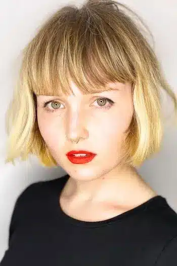 Short French bob with blunt edges on a blonde woman wearing red lipstick
