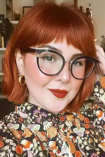 Sleek French bob with subtle texture on a woman with copper hair and glasses