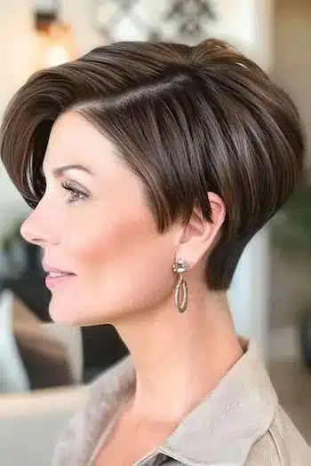 Side-parted asymmetrical wedge haircut, side view of a smiling woman with brown hair