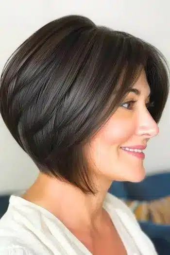 Sleek angled wedge haircut in dark brown, side profile of a smiling woman