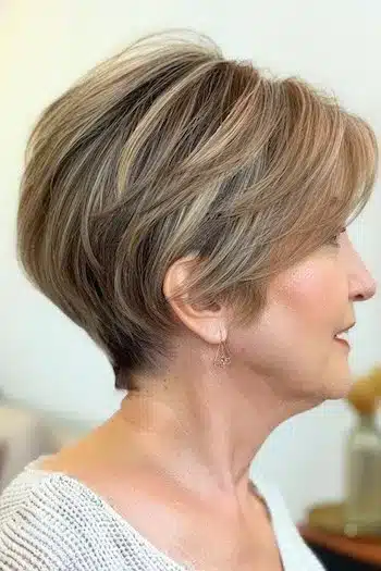 Highlighted pixie bob haircut with warm tones, side view of a smiling woman